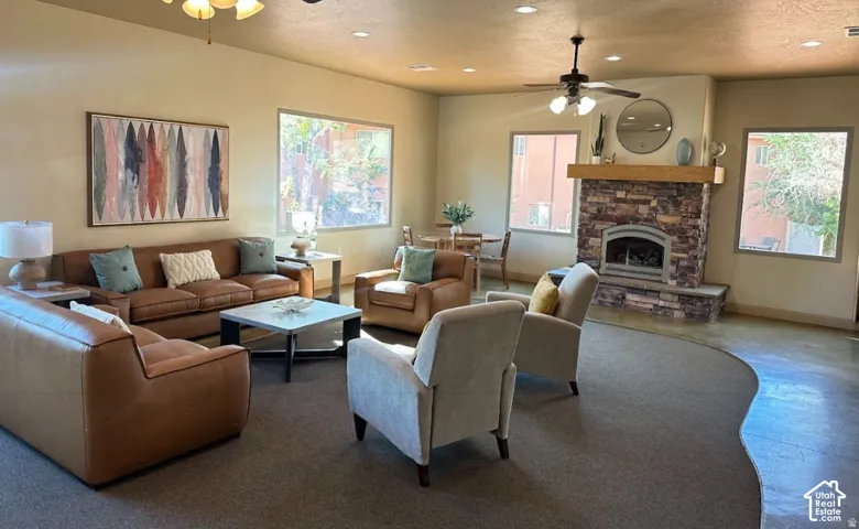 Open-concept interior featuring stone fireplace surround with wood mantel, large picture windows, recessed lighting, and ceiling fans