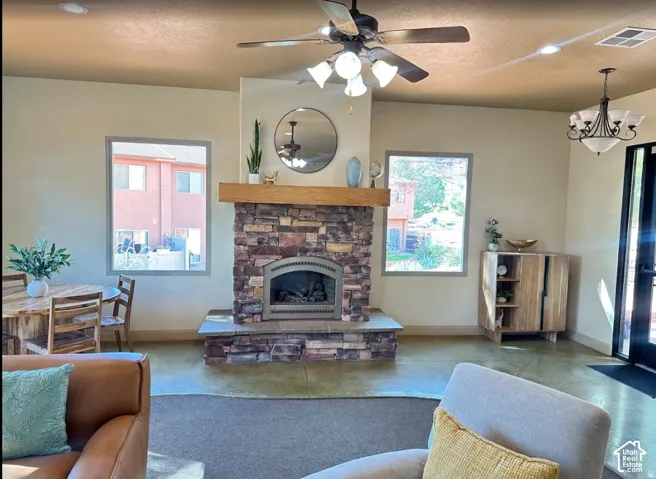 Floor-to-ceiling stone fireplace with a prominent timber mantel, recessed ceiling lighting, multi-light ceiling fan, and large picture windows