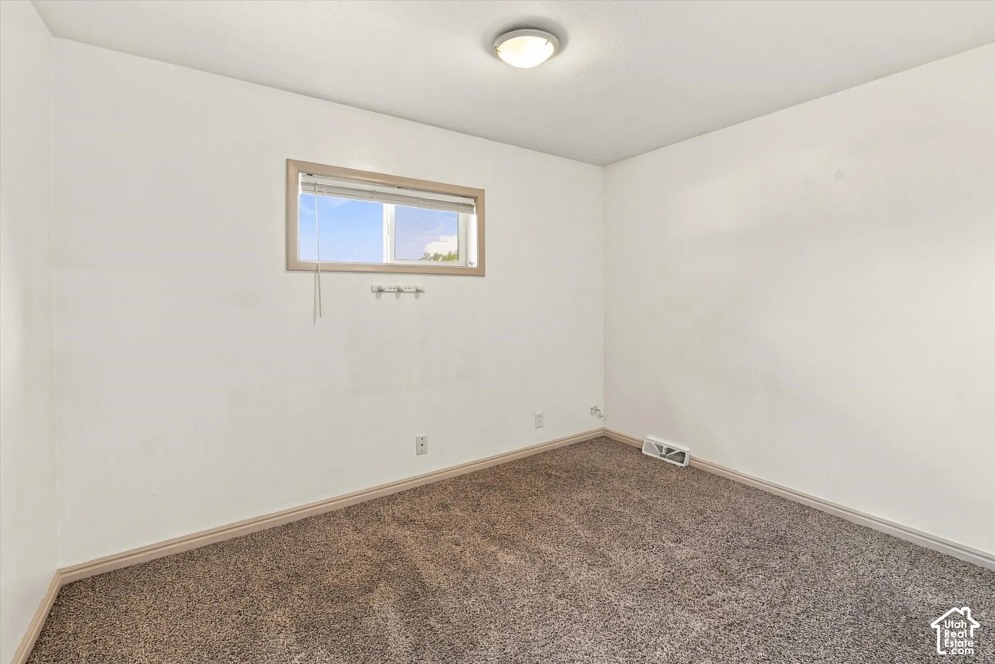 Neutral-toned wall-to-wall carpeting, clean white wall finish, rectangular single-pane window with wood-trim framing, and a central flush-mount ceiling light fixture