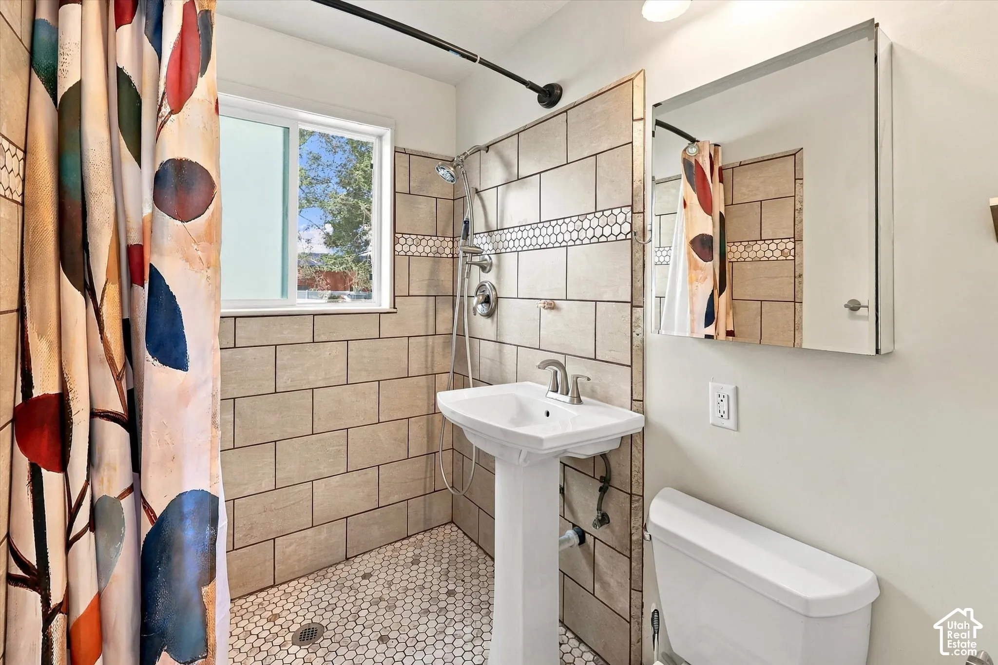 Bathroom featuring a pedestal sink with chrome faucet, hexagonal mosaic floor tile, subway-style wall tile with decorative accent border, and a mirrored medicine cabinet.  This shower features a Roll-in shower which is great for anyone with mobility chall