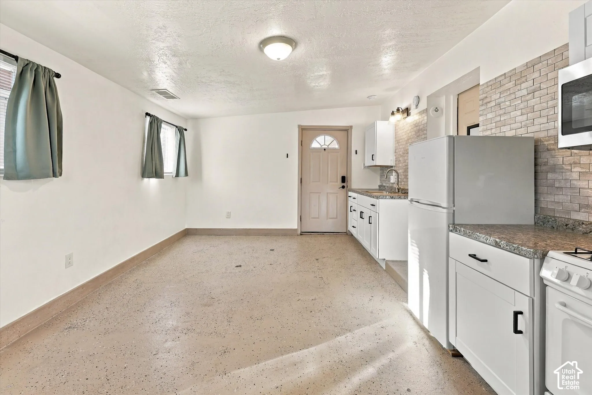 Kitchen featuring white cabinetry, stone-finish countertops, brick-style tile backsplash, and light-toned flooring.  Another view