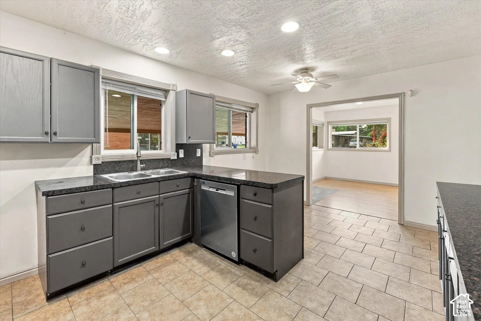 Kitchen featuring dark grey shaker-style cabinetry, stone-finish countertops, stainless steel dishwasher, dual-basin stainless steel sink, and ceramic tile flooring