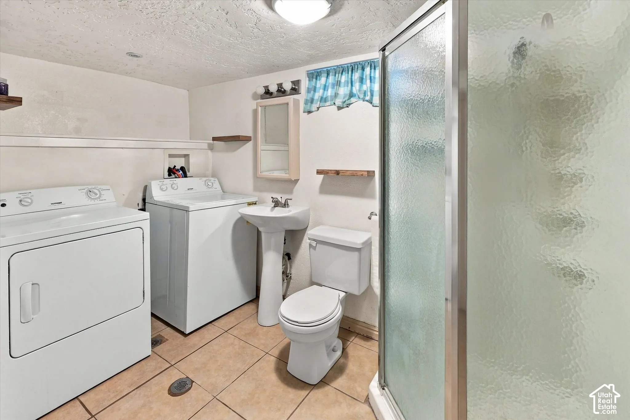 Bathroom featuring a walk-in shower with textured glass enclosure, pedestal sink, tiled flooring, and wall-mounted shelving and basement laundry for the additional dwelling.