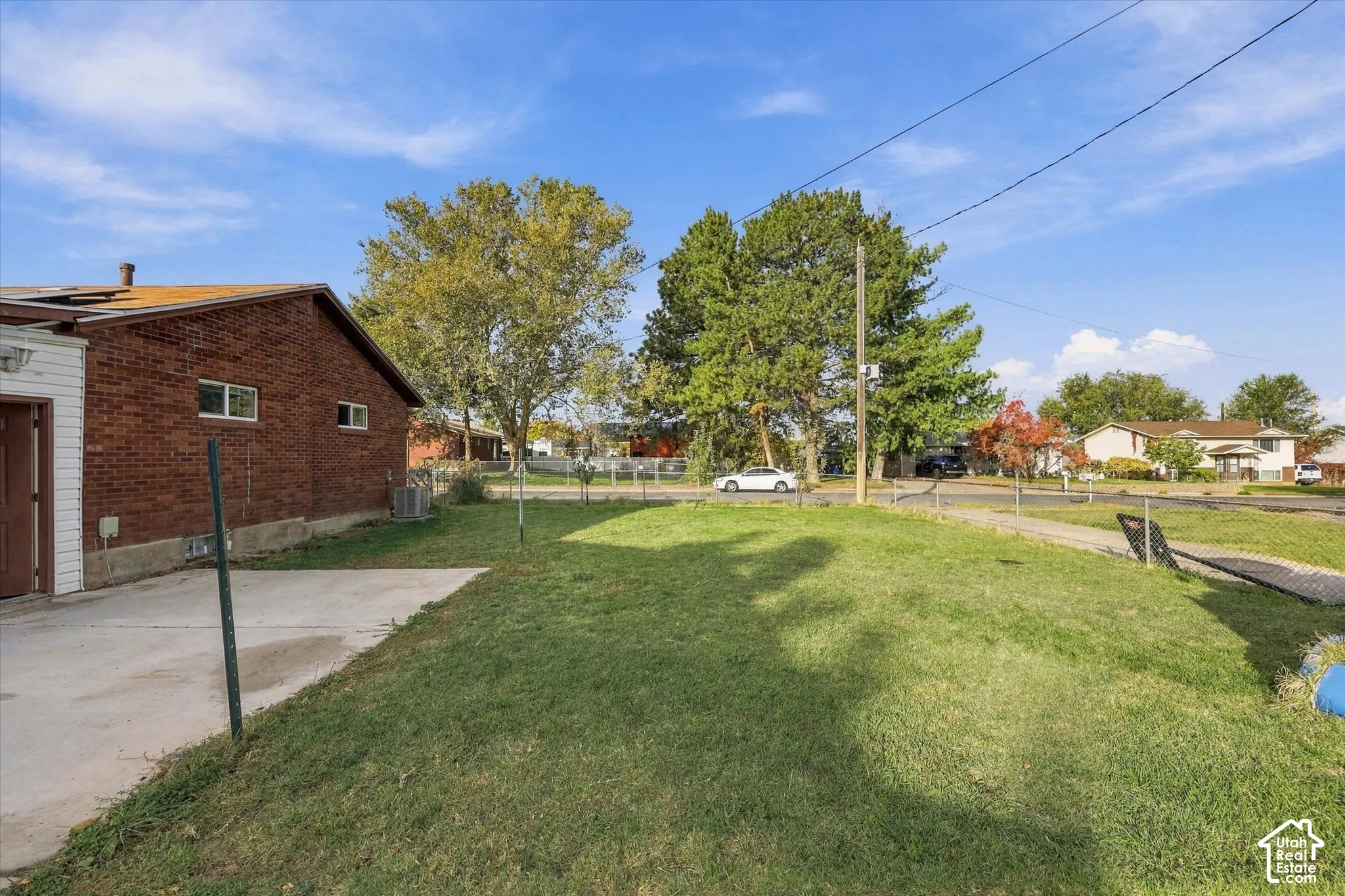 Brick exterior residence featuring a concrete patio, a chain-link fenced perimeter, and mature trees on a level lot