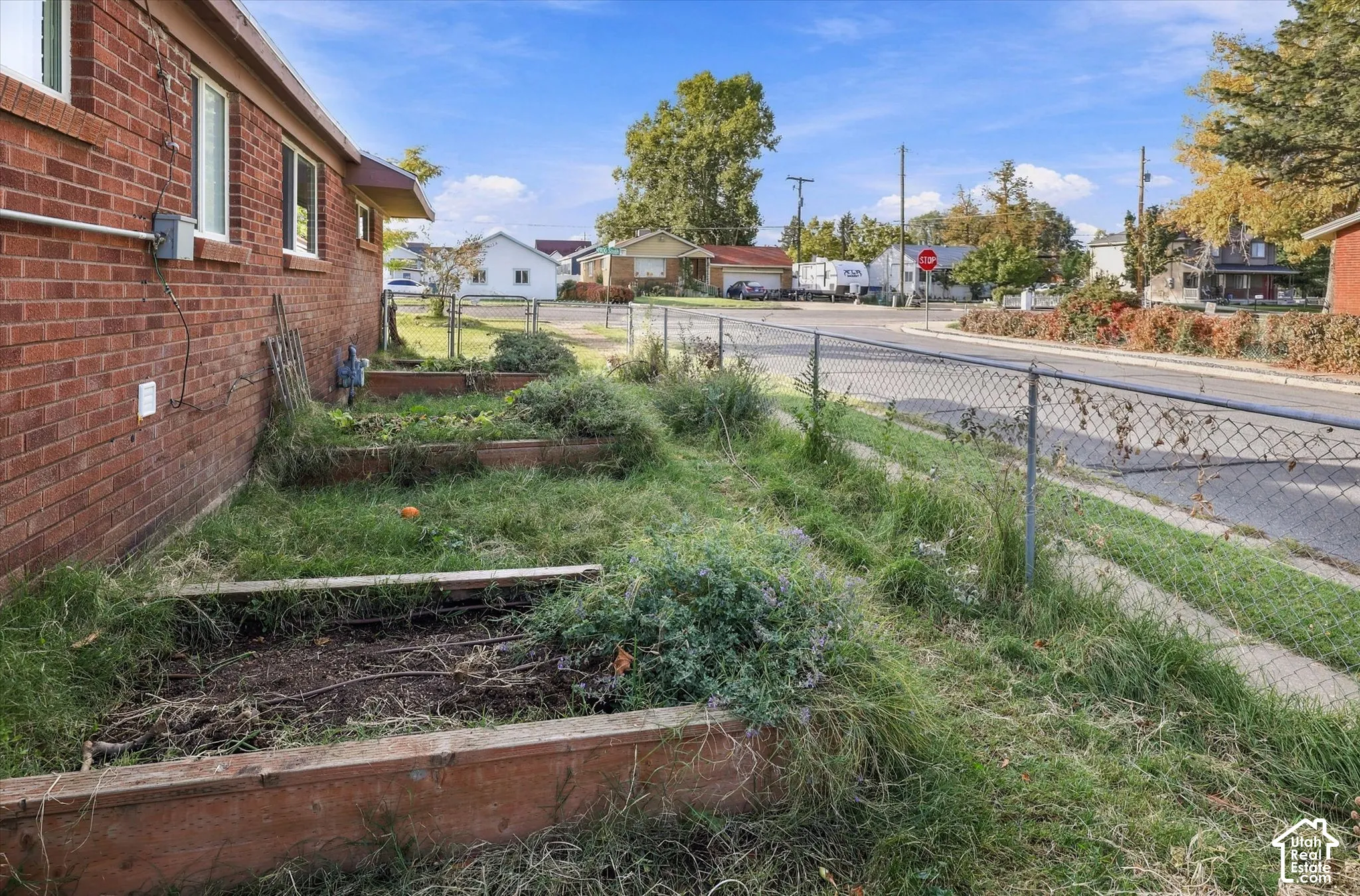 Red brick exterior featuring raised timber garden beds and a chain-link perimeter fence