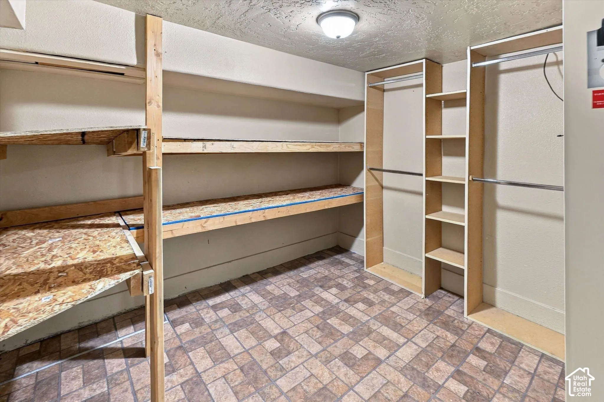 Storage area featuring integrated wood shelving units, multi-level hanging rods, and patterned tile flooring