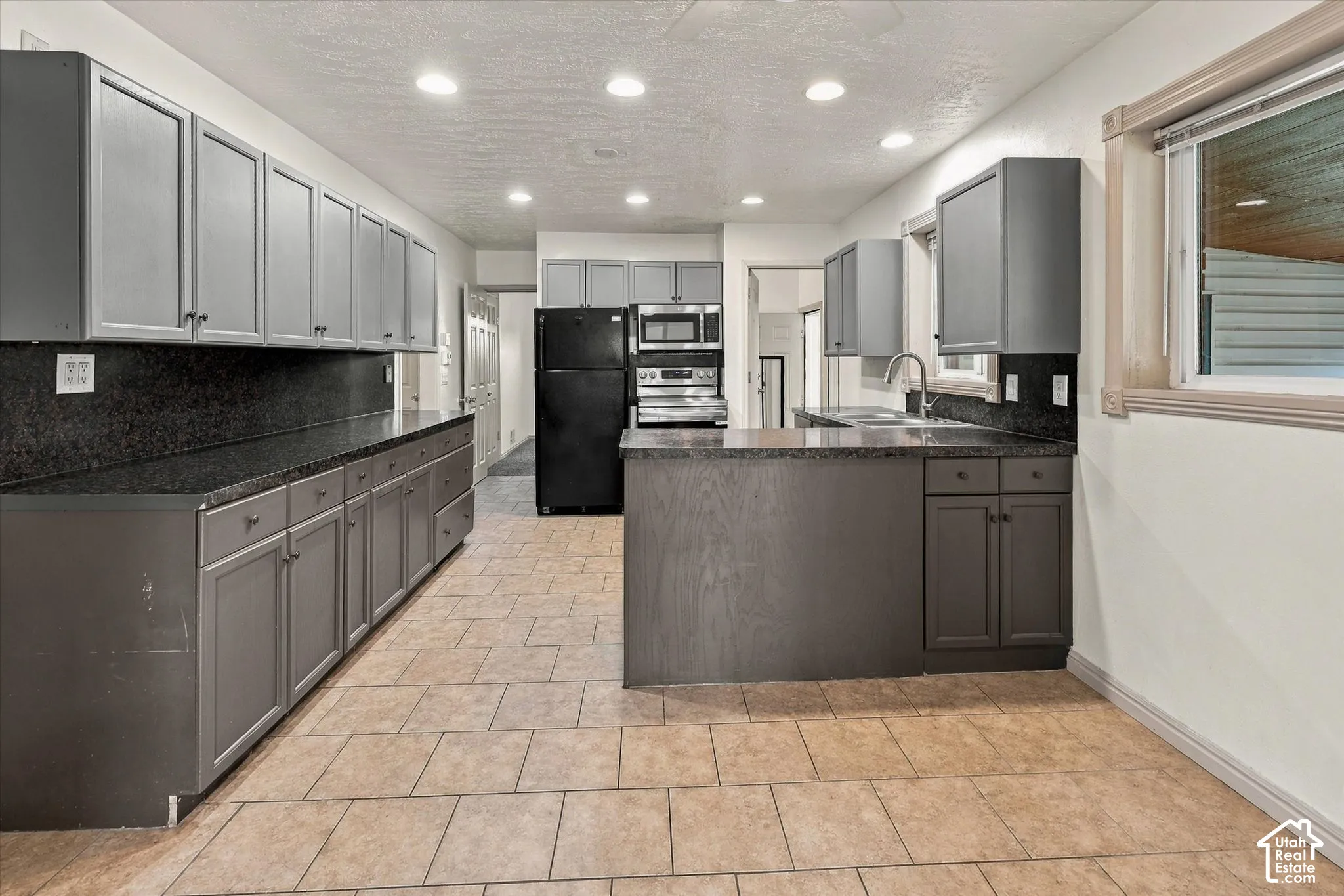 Kitchen featuring gray cabinetry, dark stone-finish countertops, tile flooring, recessed ceiling lighting, and a stainless steel undermount sink