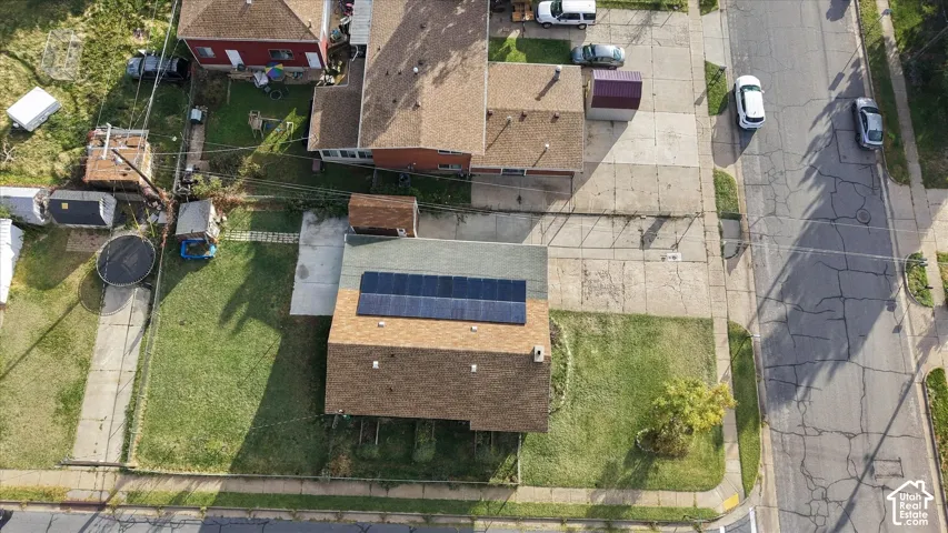 Aerial view of a residential property featuring a shingle roof with installed solar panels, a concrete driveway, and a lawn area