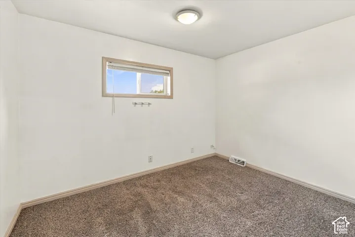 Neutral-toned wall-to-wall carpeting, clean white wall finish, rectangular single-pane window with wood-trim framing, and a central flush-mount ceiling light fixture