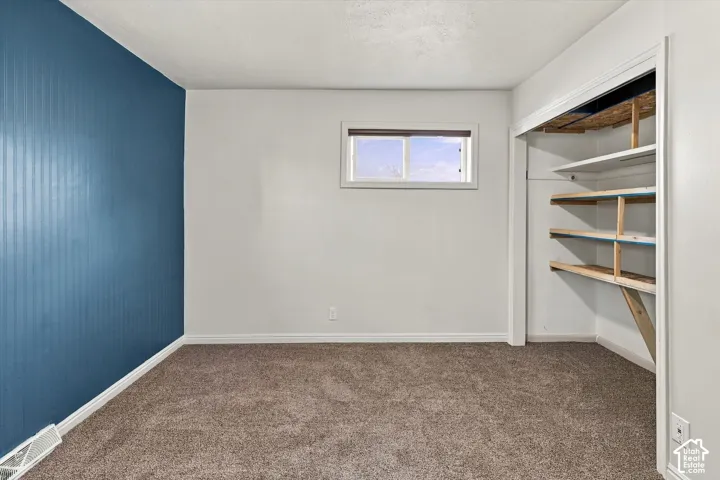 Room featuring carpeted flooring, a bold blue accent wall, a sliding-window, and an open closet with built-in wooden shelving