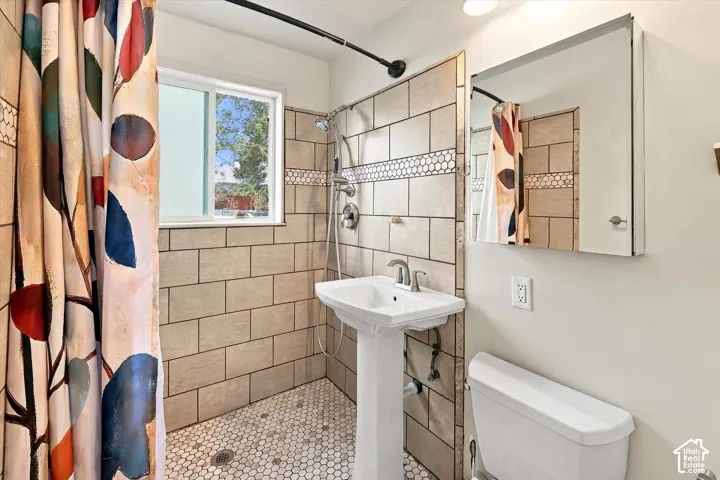 Bathroom featuring a pedestal sink with chrome faucet, hexagonal mosaic floor tile, subway-style wall tile with decorative accent border, and a mirrored medicine cabinet.  This shower features a Roll-in shower which is great for anyone with mobility chall