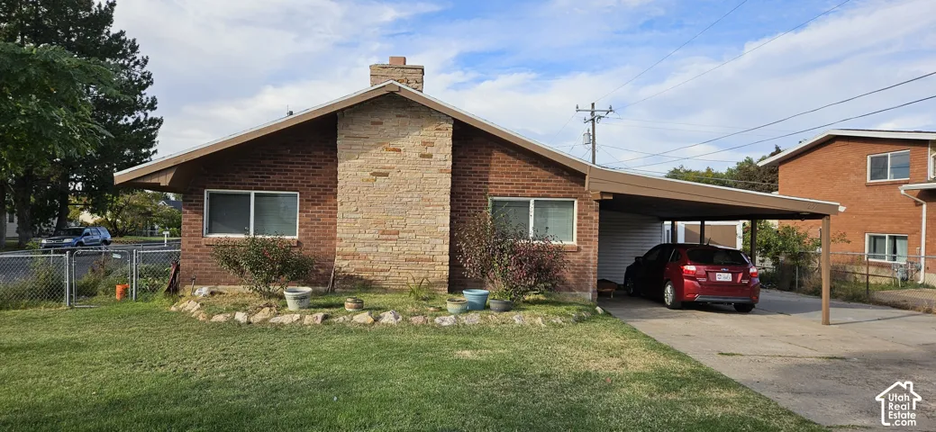 Brick exterior featuring a central natural stone chimney, low-pitch roofline, and attached carport