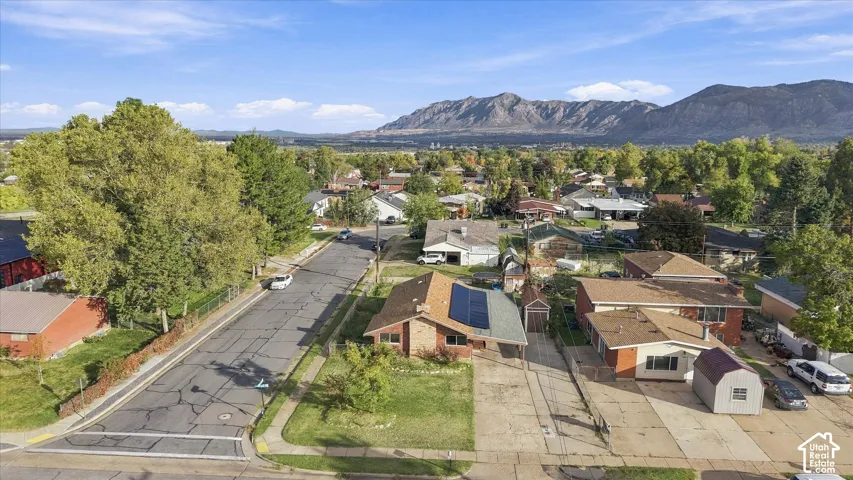 Aerial perspective featuring a brick exterior residence, installed rooftop solar panels, a concrete driveway, and expansive mountain terrain