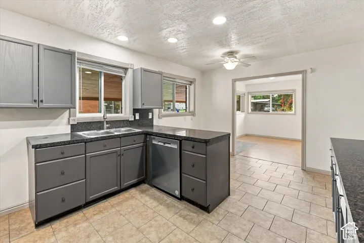 Kitchen featuring dark grey shaker-style cabinetry, stone-finish countertops, stainless steel dishwasher, dual-basin stainless steel sink, and ceramic tile flooring