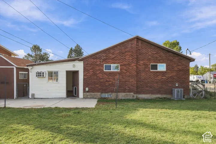 Brick and horizontal siding exterior with a concrete patio, grassy yard, and detached storage structure