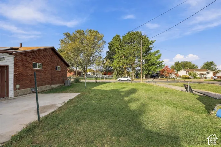 Brick exterior residence featuring a concrete patio, a chain-link fenced perimeter, and mature trees on a level lot
