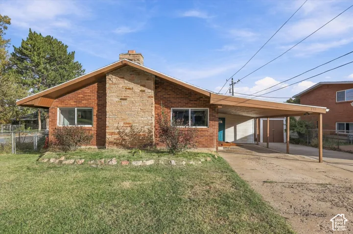 Mid-century exterior featuring brick siding, a prominent natural stone chimney, dual-pitched roofline, and an attached carport