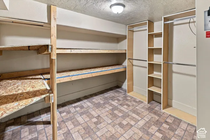 Storage area featuring integrated wood shelving units, multi-level hanging rods, and patterned tile flooring