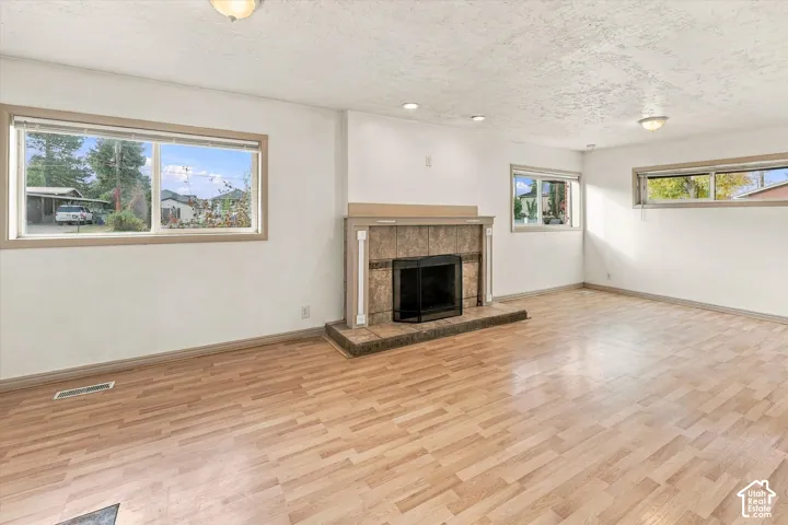 Living area featuring wood-finish flooring, three expansive windows, and a tiled fireplace surround with a raised hearth