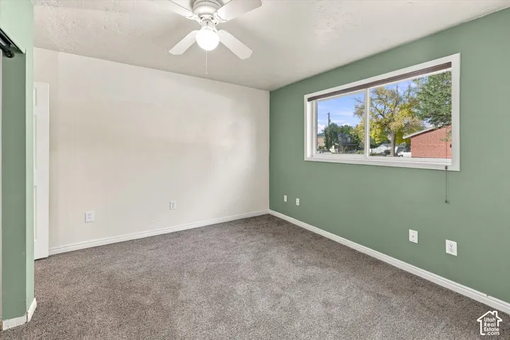 Neutral-toned carpeting, ceiling fan with integrated light fixture, and sliding glass window