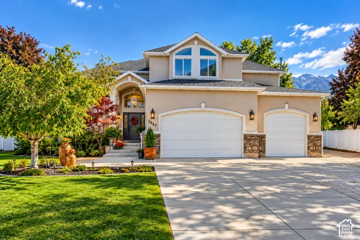 Multi-level exterior featuring stucco siding, stone veneer accents, an arched-entryway, a three-car garage, and a concrete driveway