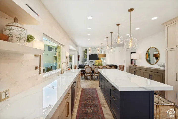 Kitchen featuring an expansive center island with waterfall-edge countertop, natural stone wall cladding, recessed lighting, glass pendant fixtures, and custom built-in cabinetry