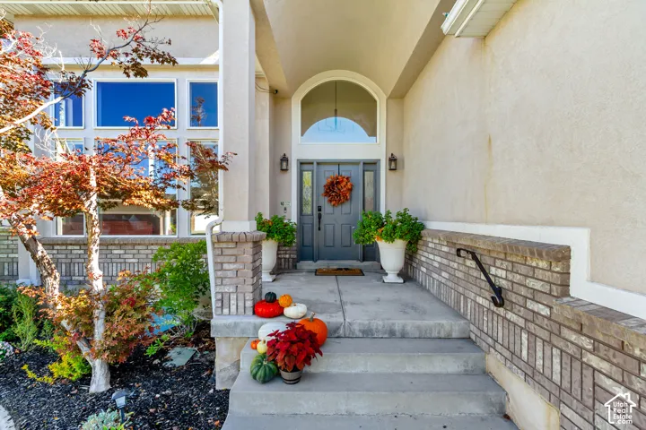Covered entryway featuring a concrete stoop, brick masonry accents, a decorative arched transom window, and a dark-toned paneled front door with flanking sidelights