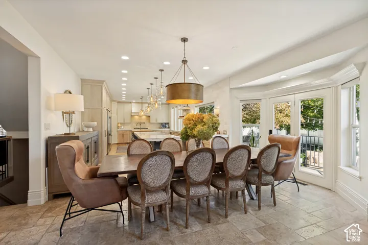 Open-concept kitchen and dining area featuring natural stone tile flooring, a chef's island, drum-style pendant lighting, and double glass doors with a bay window configuration