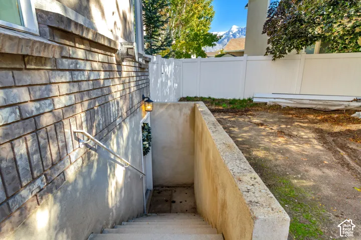 Exterior basement entrance featuring a brick facade, concrete stairwell, metal handrail, and mountain backdrop