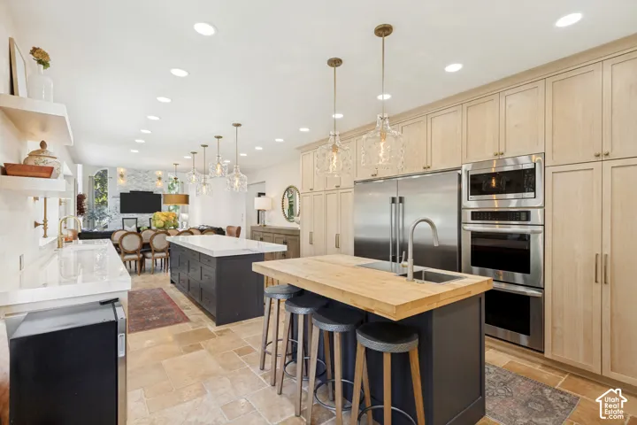 Kitchen featuring light wood-finish cabinetry, dual center islands with stone and wood-block countertops, stone tile flooring, and stainless steel built-in double wall ovens