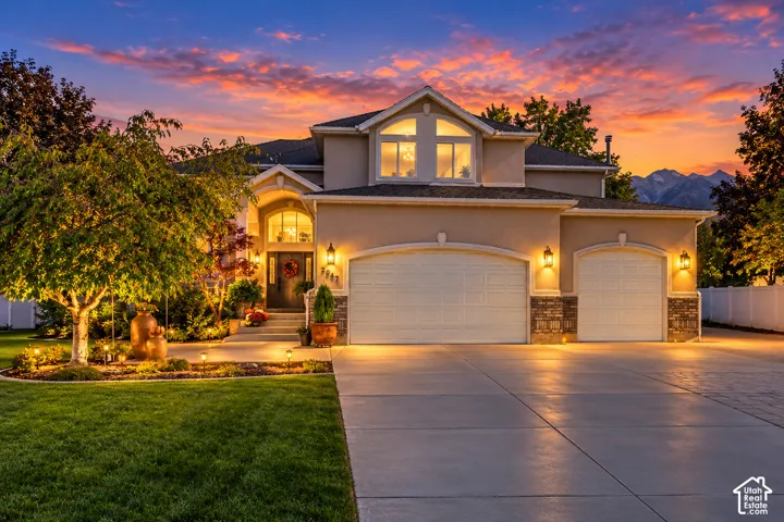 Stucco and stone exterior featuring an arched entryway, three-car garage, and upper-level arched windows against a mountain backdrop