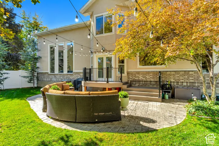Stucco and stone veneer exterior featuring a raised composite deck, stone-paver patio, and string lighting