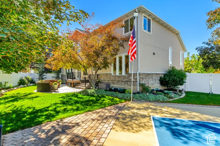 Exterior featuring stucco and stone veneer siding, a paved sport court, a stone paver patio, a raised deck with metal railings, and a vinyl privacy fence