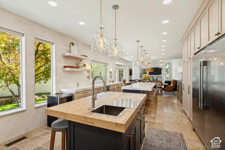 Kitchen featuring a dual-island layout with butcher block and stone countertops, natural stone flooring, custom cabinetry, stainless steel appliances, and pendant lighting