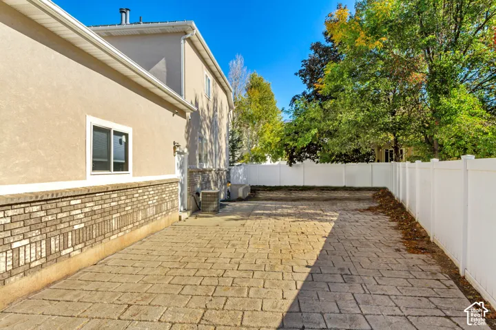 Paved stone patio featuring a brick wainscot exterior finish, white privacy fencing, and mature trees