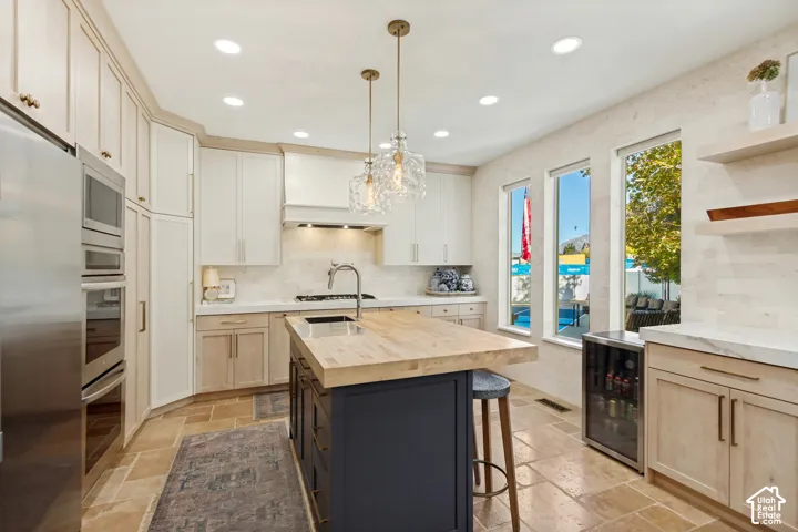 Kitchen featuring cabinetry with light wood and dark-tone finishes, wood-topped central island, stainless steel wall-mounted oven and microwave, natural stone flooring, and built-in under-counter beverage refrigerator