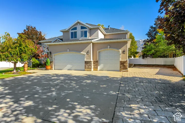 Two-story stucco exterior featuring a three-car garage, stone veneer siding accents, paved driveway, and mountain backdrop
