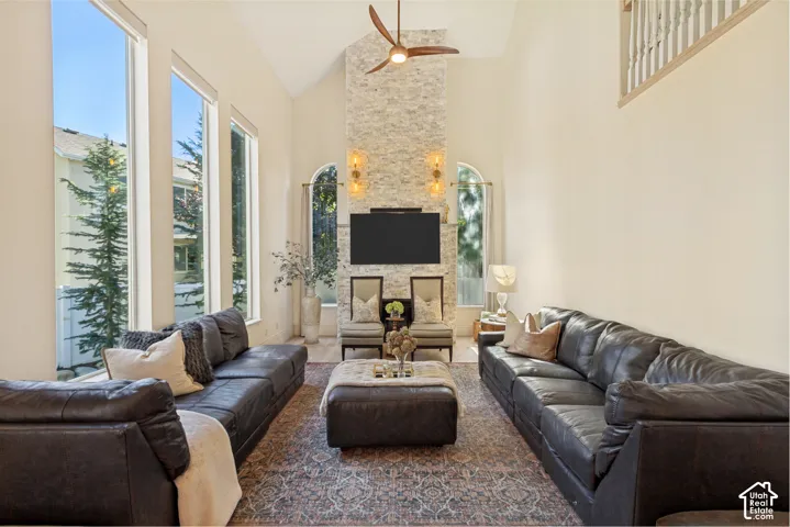 Vaulted ceilings featuring a full-height stone masonry fireplace, expansive floor-to-ceiling windows, arched windows, and a ceiling-mounted fan