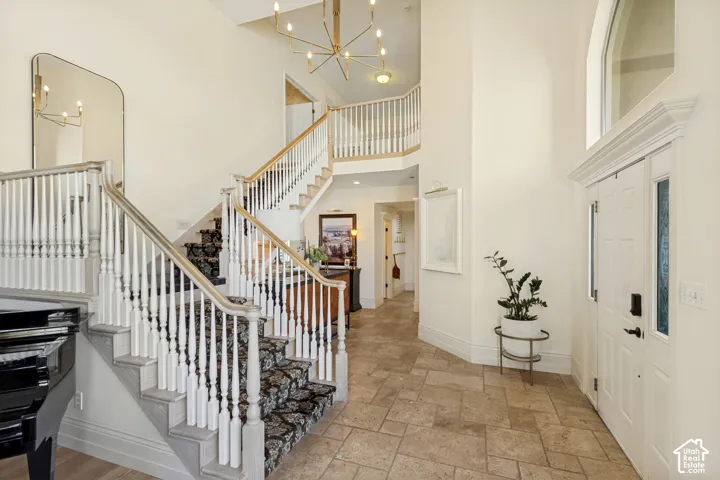 Double-height foyer featuring stone tile flooring, a prominent staircase with decorative railings, custom multi-arm chandelier, and an arched window above the entry door