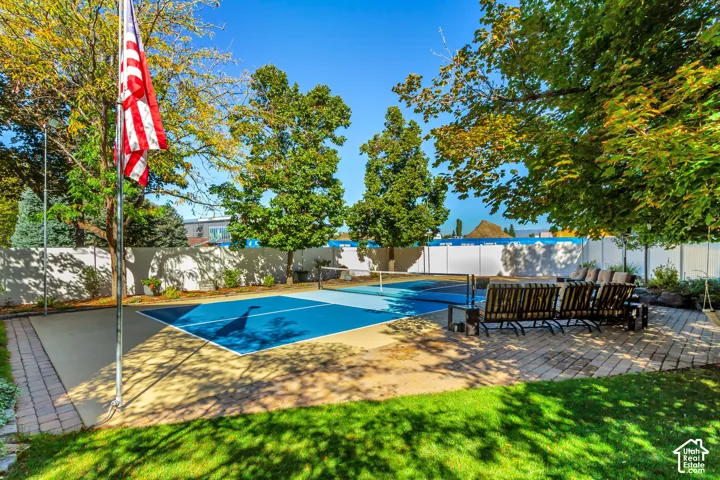 Sport court featuring a multi-colored surface, surround fencing, brick paver patio, and mature trees