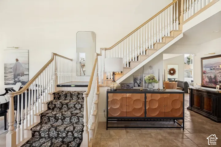 Two-story foyer featuring tile flooring, a staircase with patterned carpeting, white balusters, and a natural wood-finish handrail
