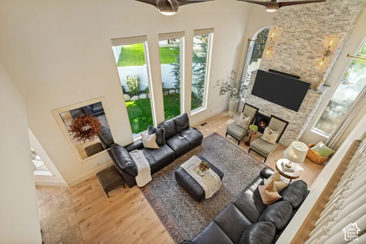 High-ceiling living room featuring stone-clad fireplace surround, light wood-finish flooring, floor-to-ceiling windows, and dual ceiling fans