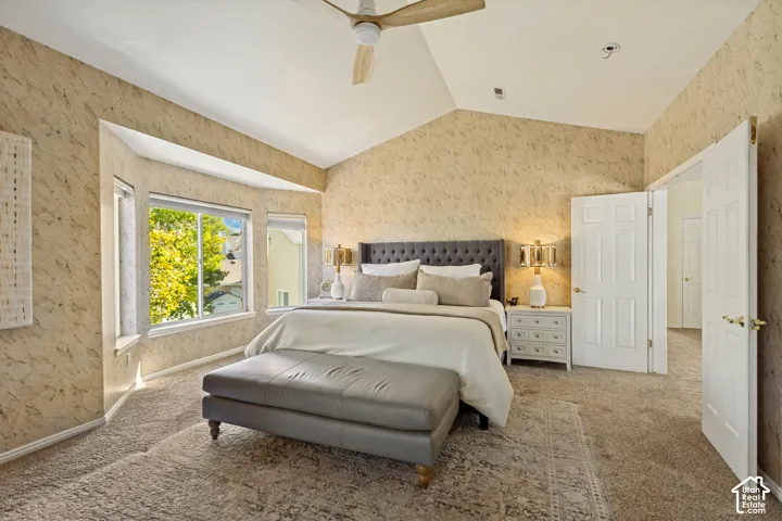 Vaulted ceiling featuring a central multi-blade paddle fan, bay window, and neutral-toned wall covering