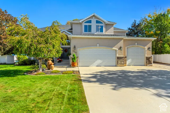 Multi-level exterior featuring a combination of stucco and stone veneer siding, an arched window gable, a three-car garage, and a concrete driveway