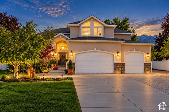 Stucco exterior featuring stone veneer accents, a triple-bay garage, arched entryway, and mountain backdrop