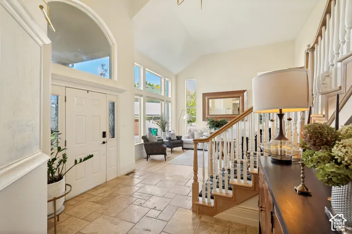 Foyer featuring vaulted ceilings, arched transom window, large-format tile flooring, and a wooden staircase with white balusters