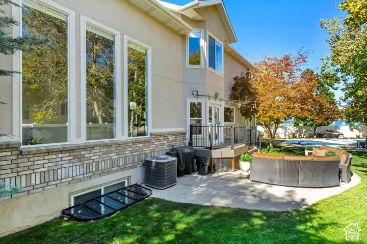 Exterior featuring stucco siding with stone veneer accents, an expansive rear patio, elevated deck with metal railing, and large vertical windows
