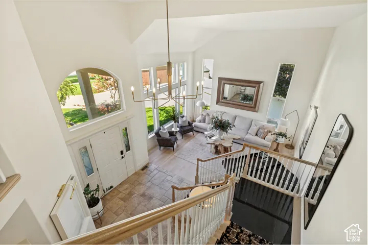 Vaulted ceilings, expansive multi-pane windows, stone-finish flooring, a linear staircase featuring white balusters with a light-tone wood handrail, and a tiered metal chandelier