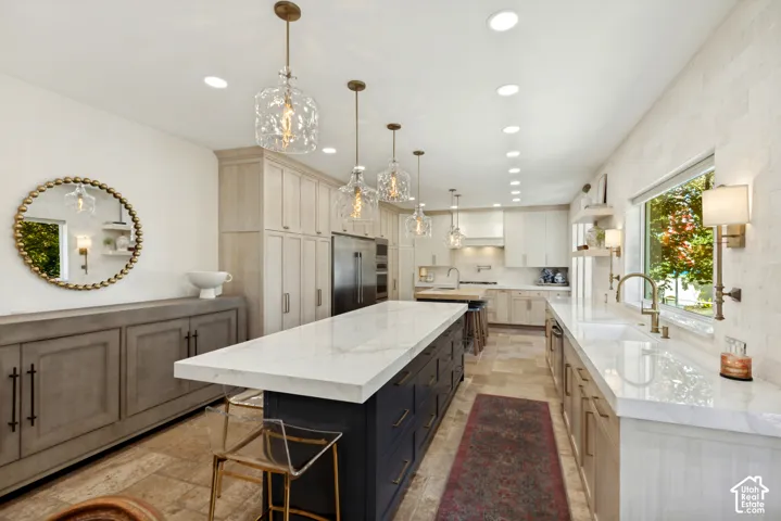 Kitchen featuring a large central island with a stone-finish countertop, custom cabinetry, recessed lighting, glass pendant fixtures, and stone-tile flooring