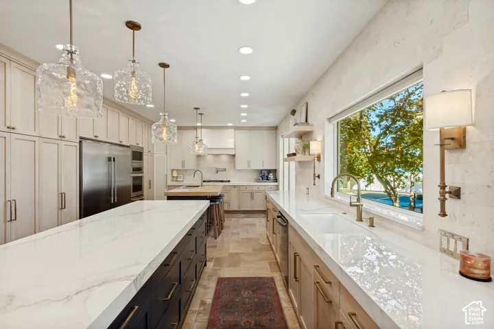 Kitchen featuring light-toned cabinetry, a dark-toned central island with a quartz countertop, stone tile backsplash, stone tile flooring, and integrated stainless steel appliances